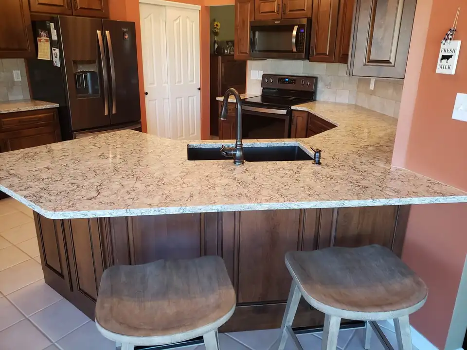 Light granite peninsula countertop with an undermount sink and two bar stools on cherry cabinets: countertop installation by Danny's Top Shop in Festus, MO