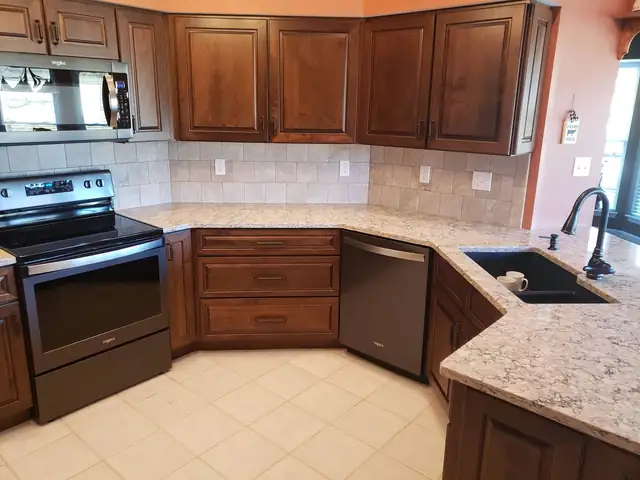Light granite countertops on cherry kitchen cabinets with a tile backsplash and an undermount sink