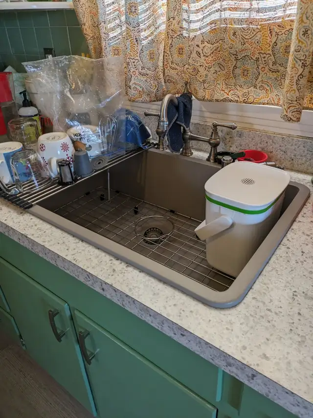 Large taupe granite composite kitchen sink with a stainless rack set into a speckled countertop